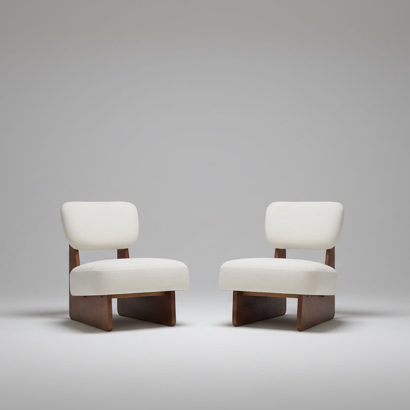 Two white chairs with wooden legs in a room with a plant and clock on the wall.