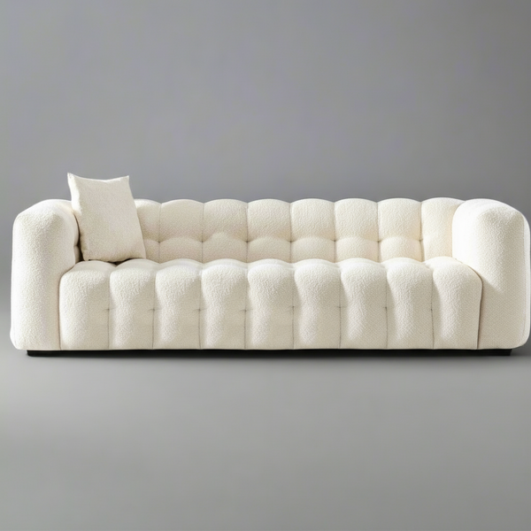 White tufted sofa with a single pillow against a gray background