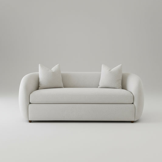 White sofa with white cushions in a room with plants and a wooden coffee table.